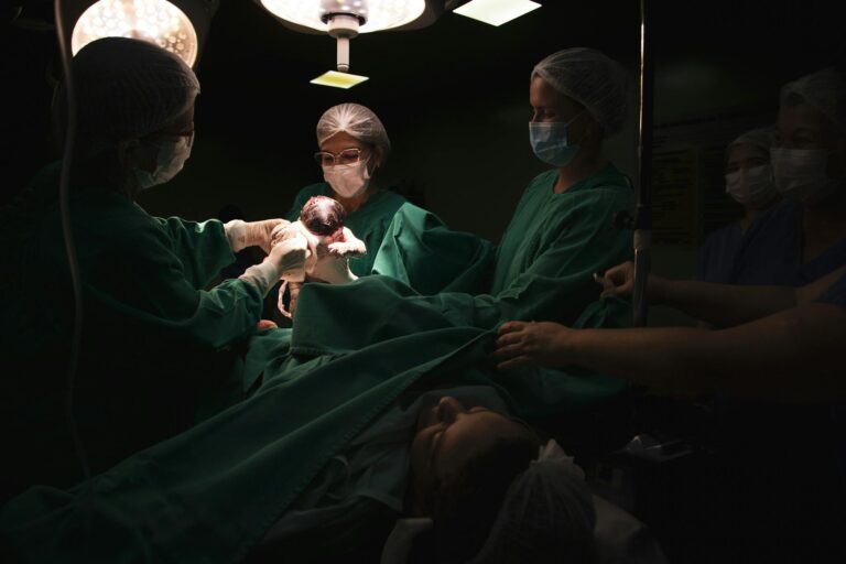 A medical team assists a childbirth in a dimly lit hospital operating room.