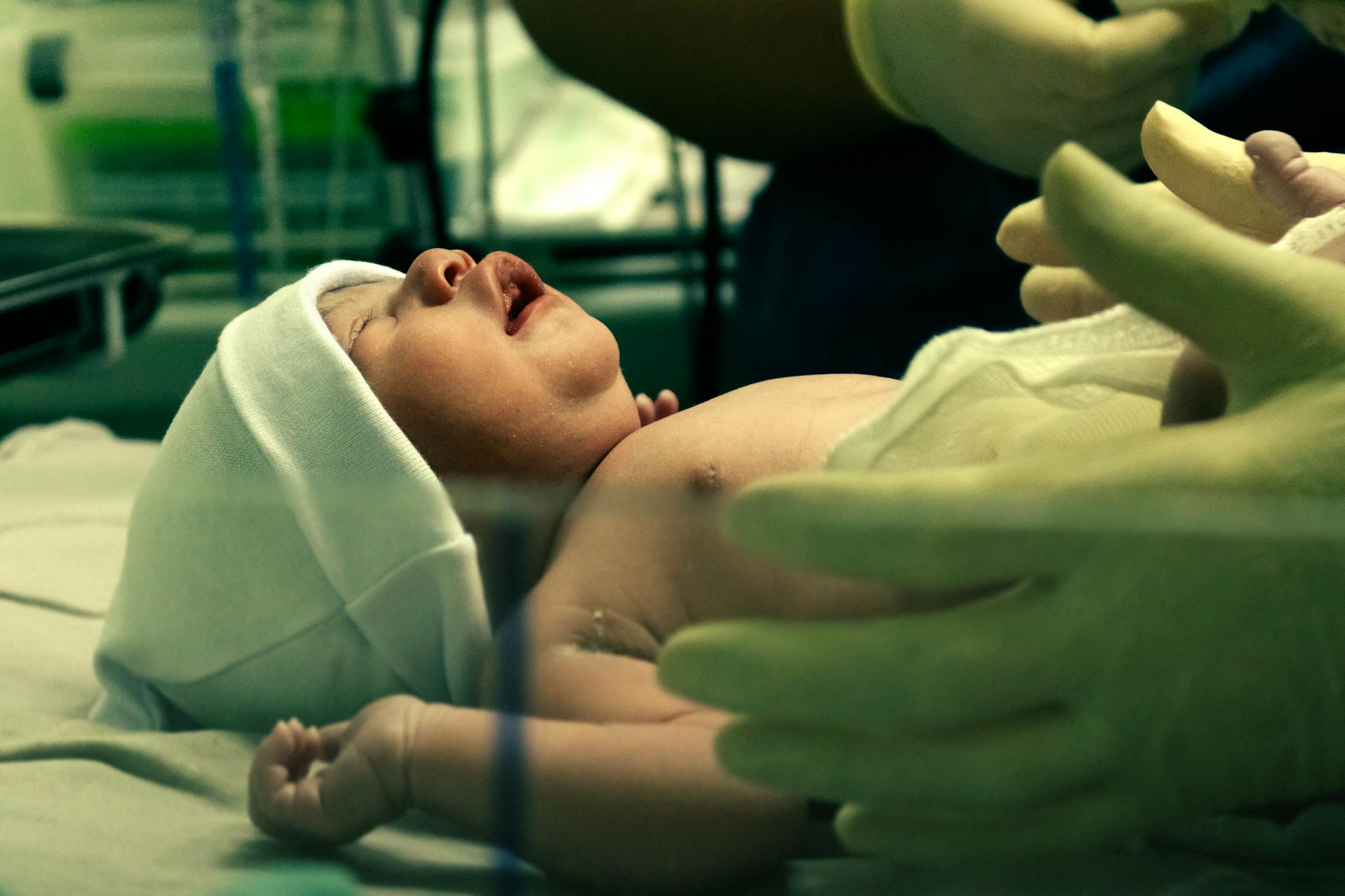 A newborn baby being gently handled by a nurse in a hospital setting.