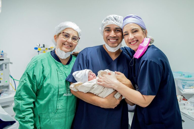 Smiling healthcare professionals holding a newborn baby in a hospital room.